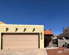 Eine Garage mit Wohnnutzung, einer beigen Tür, einer Steinmauer mit Tor und einem strahlend blauen Himmel.