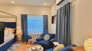 Una habitación de hotel con cama, sofá, sillón, una mesita y una lámpara.