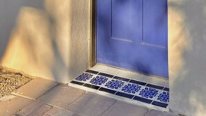 Una puerta azul con un ventanal, una luz adosada a la pared y un escalón de entrada con azulejos.