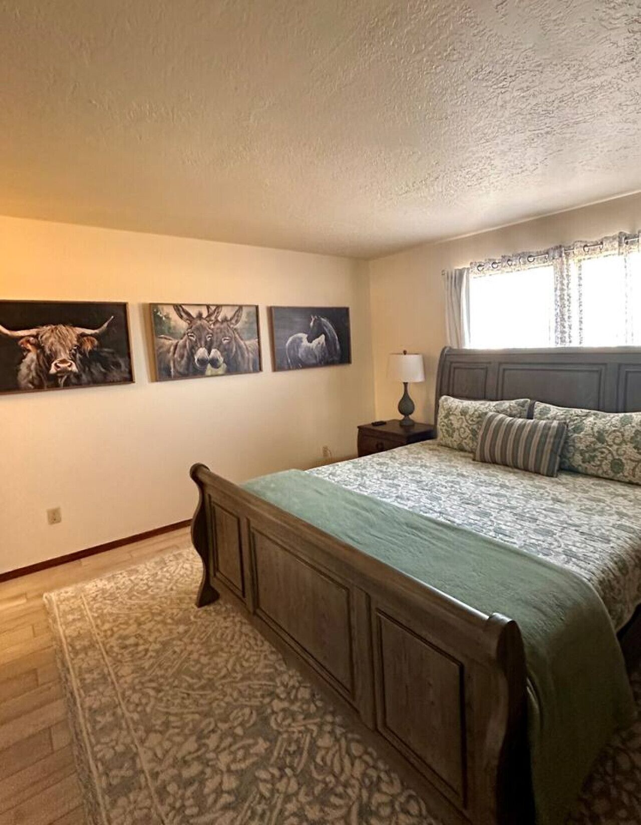 Une chambre à coucher comprenant un lit, une table de chevet, une lampe et trois tableaux représentant des animaux, accrochés au mur.