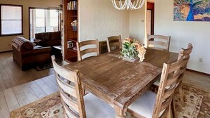 Une salle à manger avec une table et des chaises en bois, un lustre, une bibliothèque et un tableau représentant un paon accroché au mur.