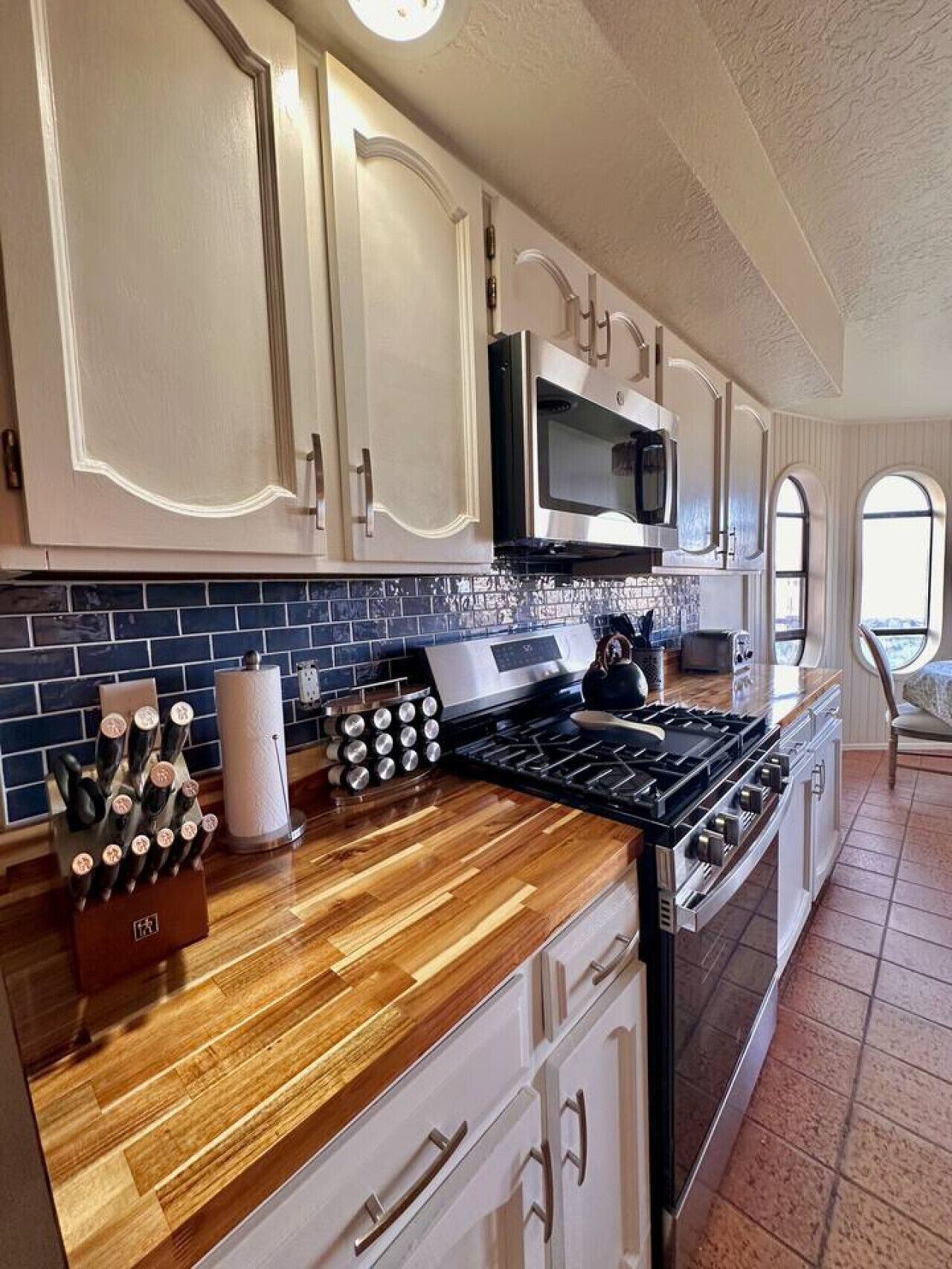 A kitchen with white cabinets, a microwave, a stove, and a knife block.