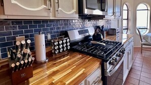 Une cuisine avec des meubles blancs, un four à micro-ondes, une cuisinière et un bloc à couteaux.