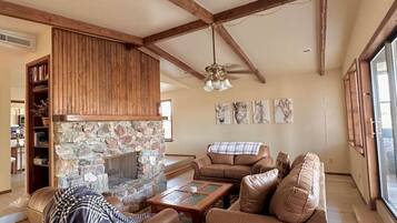 A living room with a stone fireplace, leather sofas, a glass coffee table, and wooden beams on the ceiling.
