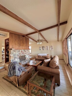 A living room with a stone fireplace, leather sofas, a glass coffee table, and wooden beams on the ceiling. - Come for the peacocks stay for the view! (Las Cruces)