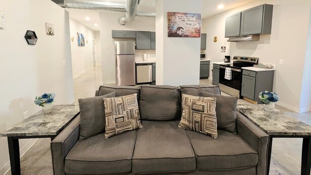 A modern living room with a grey sofa, a coffee table, and a kitchen in the background. - Novel King Suite- Central West End near SLU 101 (St. Louis)
