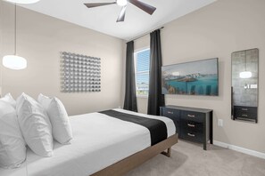 A bedroom with a bed, a ceiling fan, a wall-mounted TV, a dresser, and a window with curtains. - Upstay - Lively Mansion w Pool, Theater, Games (Kissimmee)