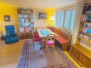Eine gemütliche Leseecke mit Holztisch, Stühlen, einer Bank und einem Bücherregal voller Bücher.