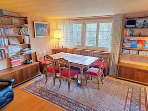 Een gezellige kamer met een houten tafel, stoelen, een boekenkast en een raam met gordijnen.