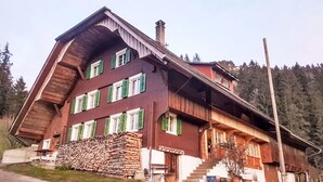 Una casa a più piani in legno, con tetto spiovente, un camino e una pila di legna davanti.
