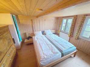 Ein Schlafzimmer einer Holzhütte mit Bett, Schminktisch und Vorhängen.