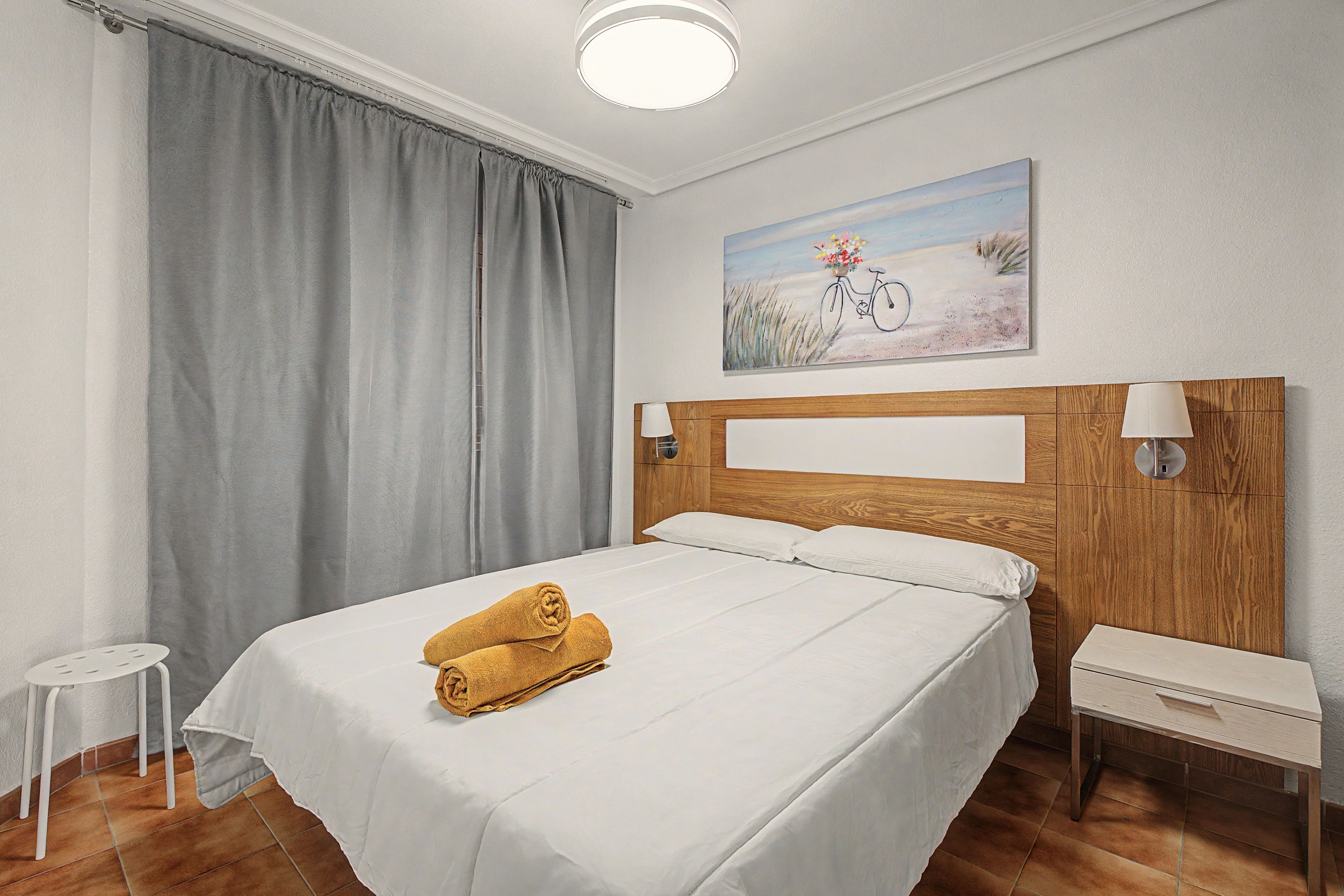 A hotel room with a bed, a nightstand, a lamp, a painting, and a window with curtains.