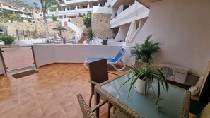 Un balcon avec un fauteuil en osier, une table en verre et un pot de fleurs.