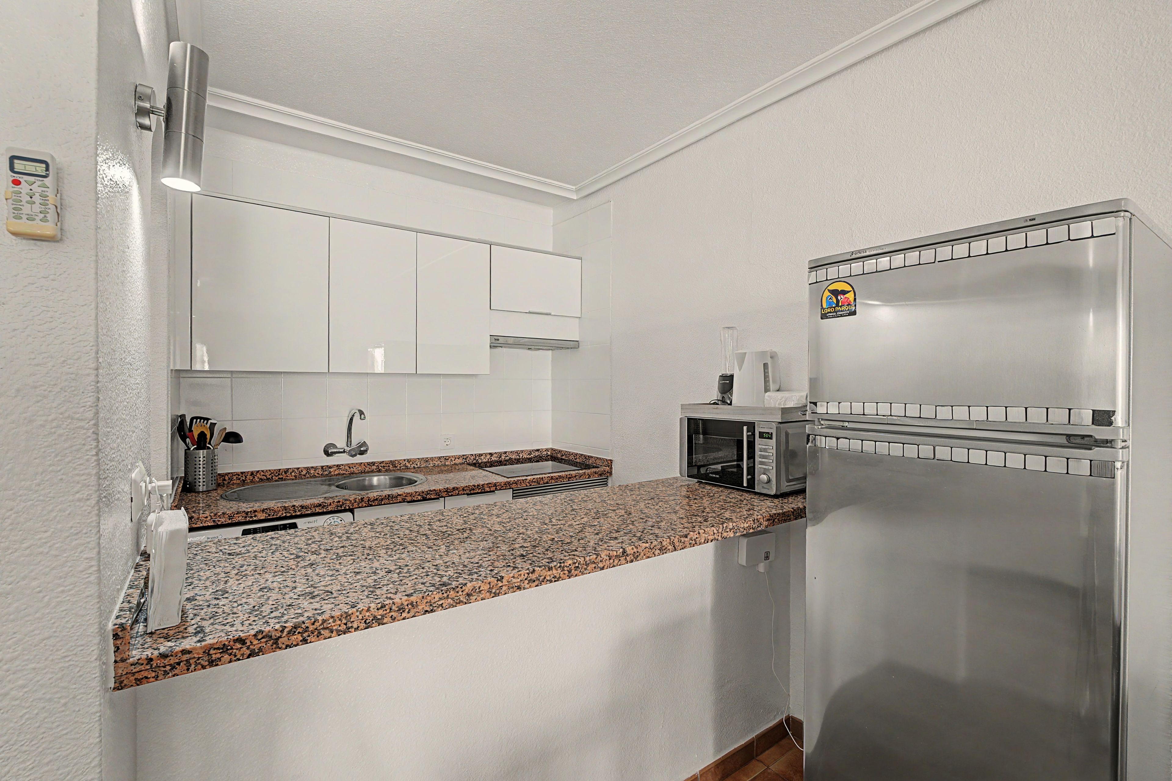 Una cocina con un refrigerador de acero inoxidable, microondas, un lavamanos y encimera de granito.