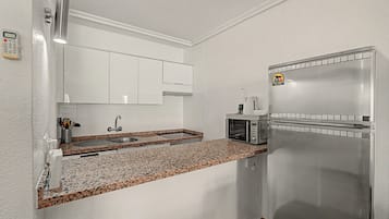Una cocina con un refrigerador de acero inoxidable, microondas, un lavamanos y encimera de granito.