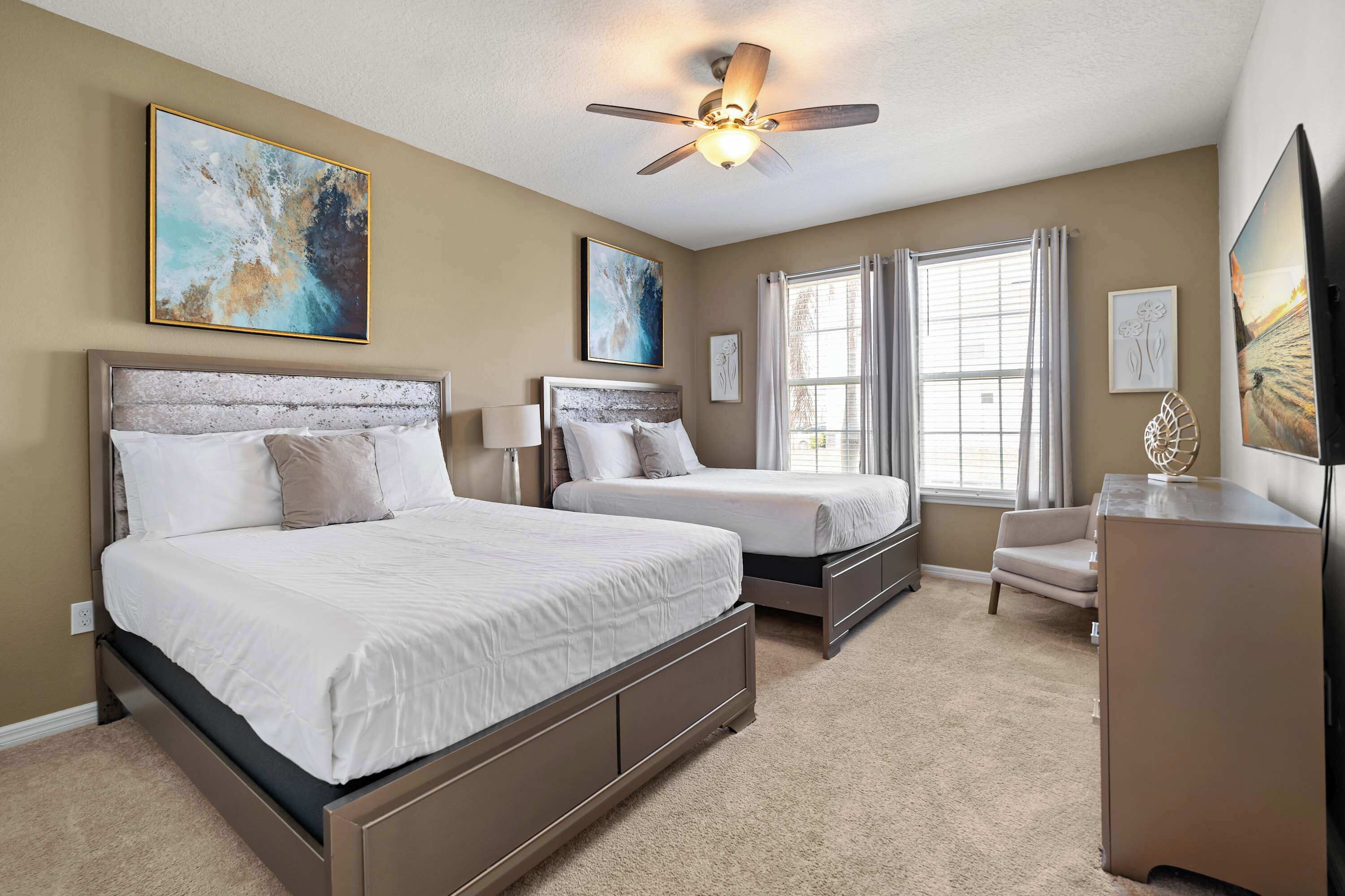 A bedroom with two beds, a ceiling fan, and artwork on the walls.