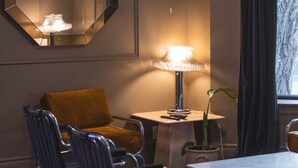 Een kamer met een grote spiegel, een tafel met een lamp, twee stoelen en een raam met gordijnen.