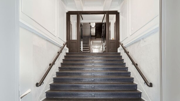 Een statige trap met een leuning, leidend naar een plateau met uitzicht op het interieur.