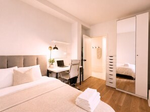 Une chambre à coucher comprenant un lit, un bureau, une chaise, une armoire et un miroir.