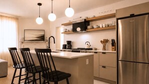 Een moderne keuken met een centraal eiland, barstoelen, een roestvrijstalen koelkast en hanglampen.