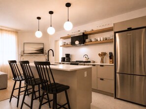 Une cuisine moderne dotée d’un îlot central, de tabourets de bar, d’un réfrigérateur en acier inoxydable et de luminaires suspendus.