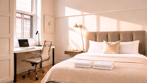 Een slaapkamer met een bed, een bureau met een laptop, een stoel, een nachtkastje met een lamp en een wandlamp.