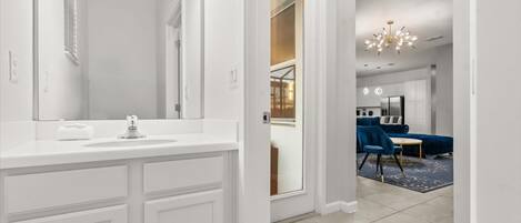 Un baño moderno con tocador blanco, un espejo grande y zona de ducha.