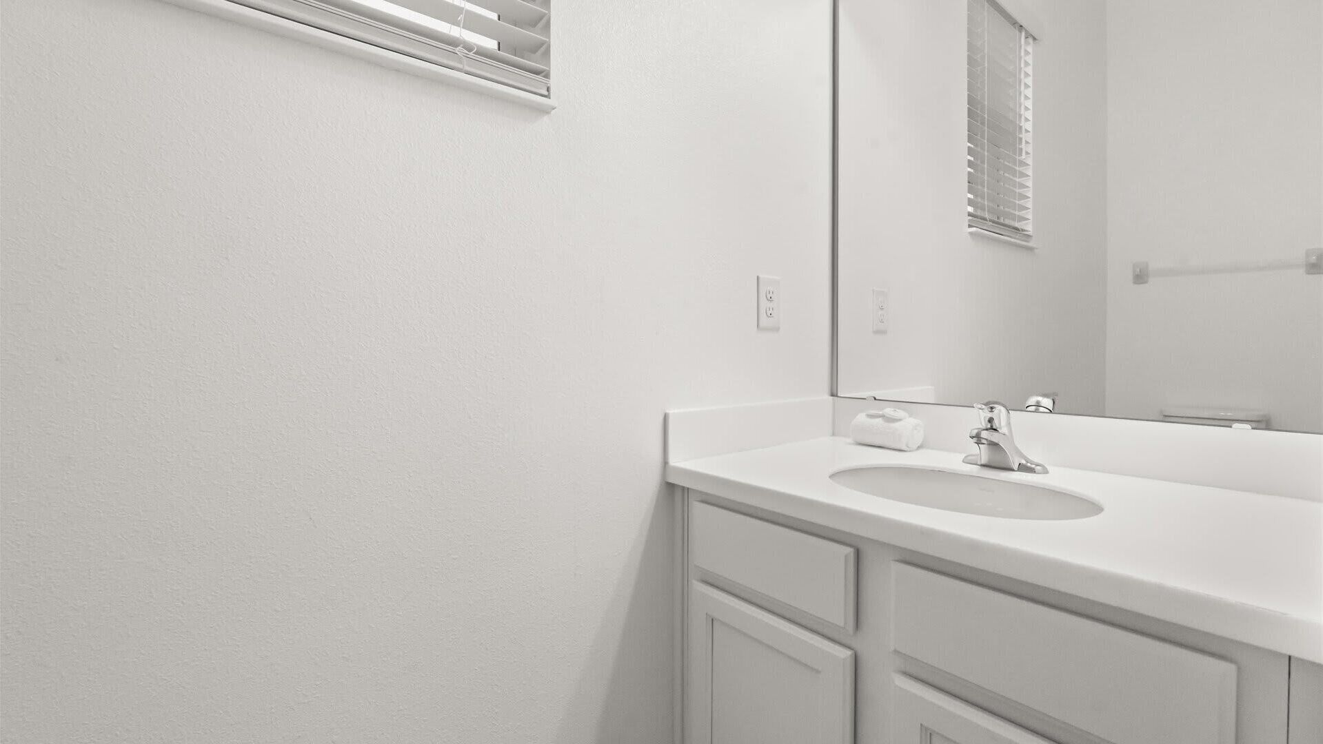 A bathroom with a white sink, a mirror, and a window with blinds.