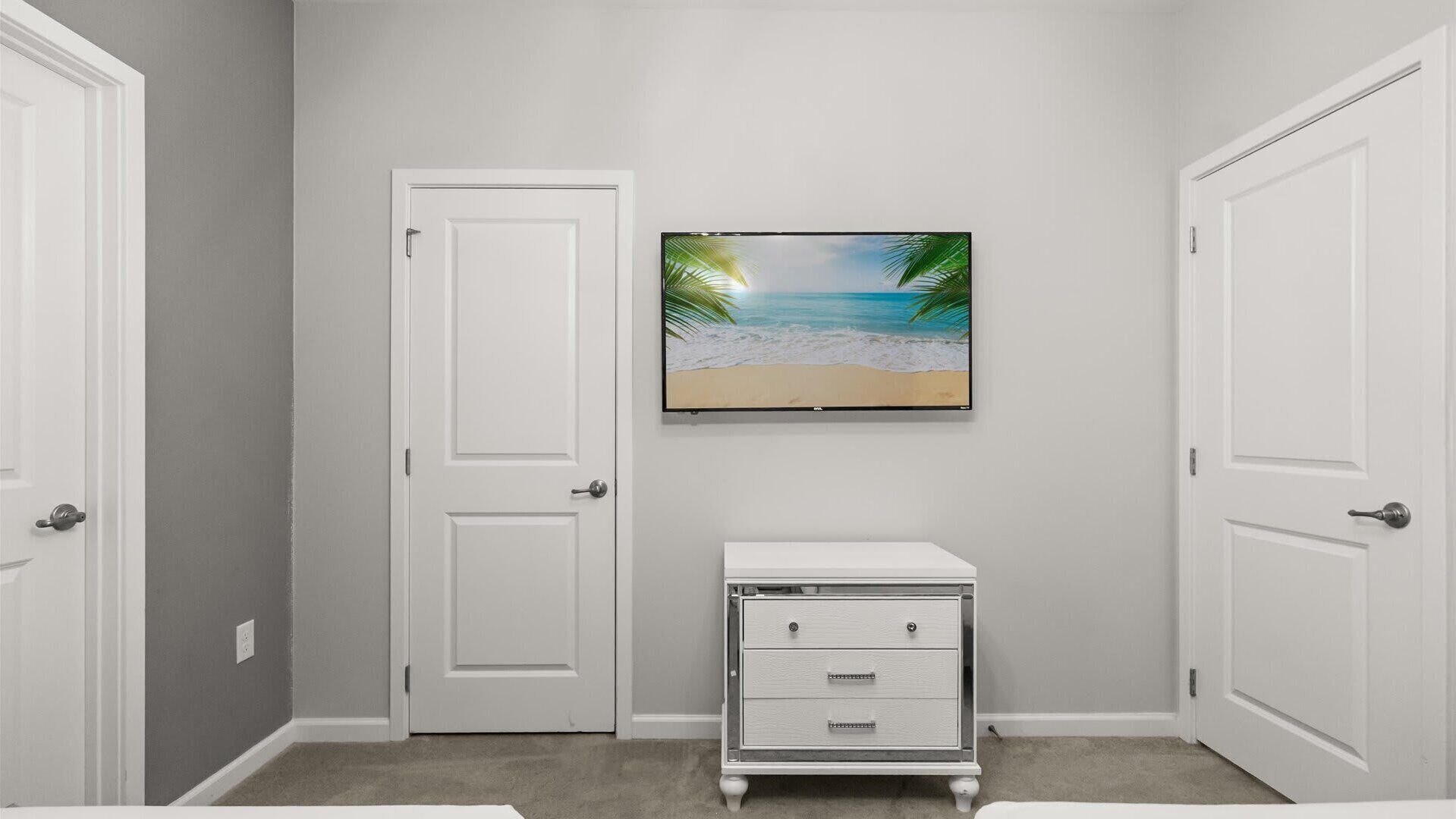 A room with a white door, a white dresser, and a framed picture of a beach scene on the wall.