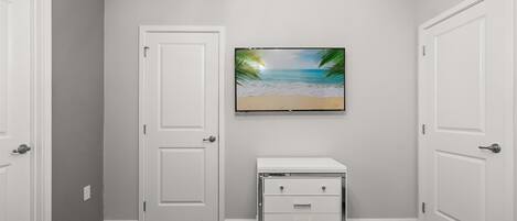 A room with a white door, a white dresser, and a framed picture of a beach scene on the wall.