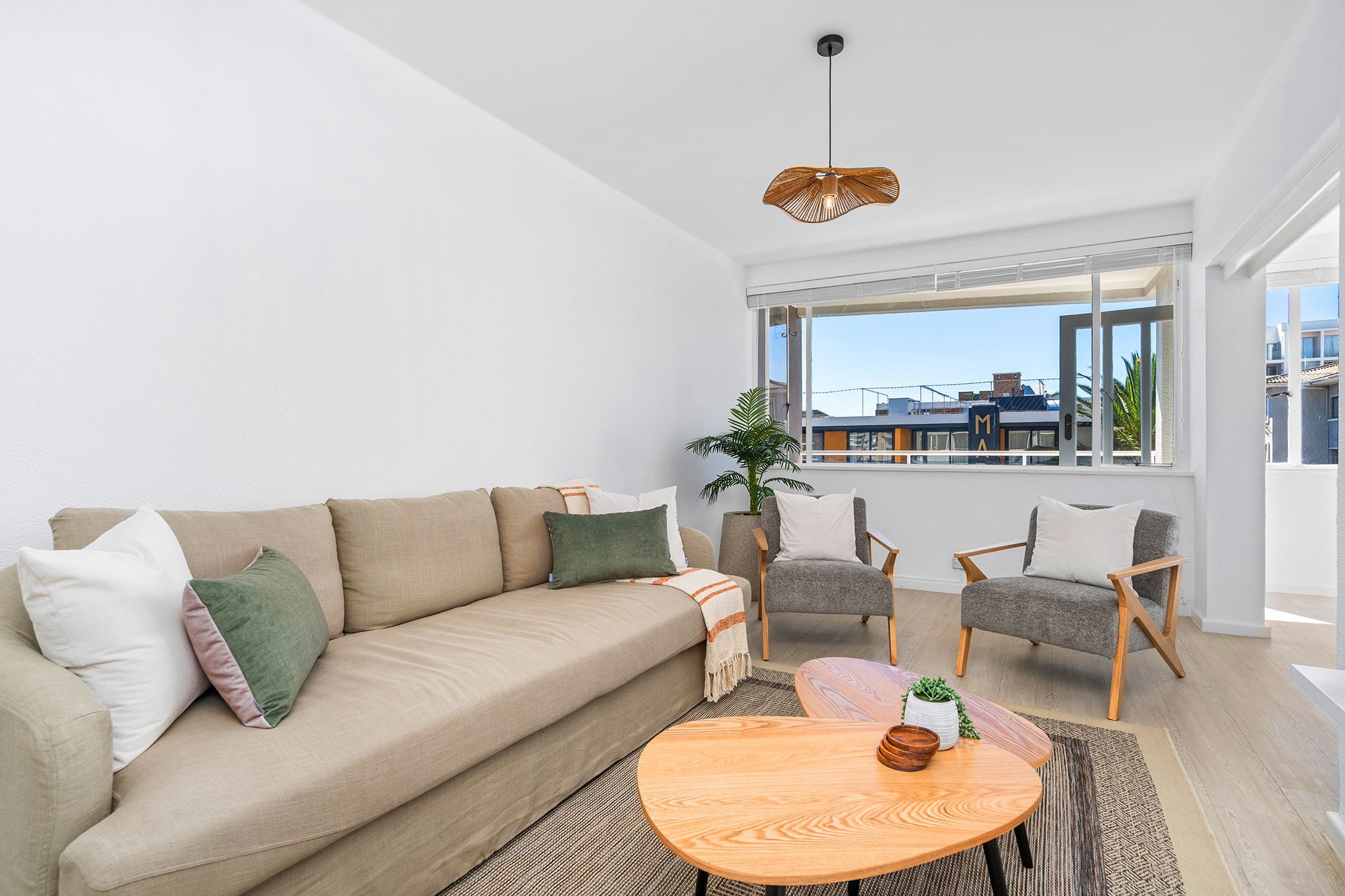 A modern living room with a sofa, armchairs, a coffee table, and a large window offering a view of buildings.