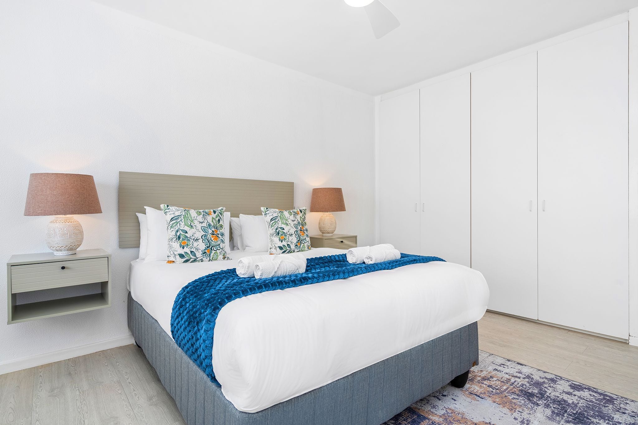 Ein modernes Hotelzimmer mit einem großen Bett, zwei Nachttischlampen, einem Nachttisch und einem Kleiderschrank.
