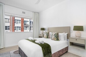 A hotel room with a large bed, two bedside tables, a window with a view of buildings, and a green throw blanket. - Monreith 406 (Cape Town)