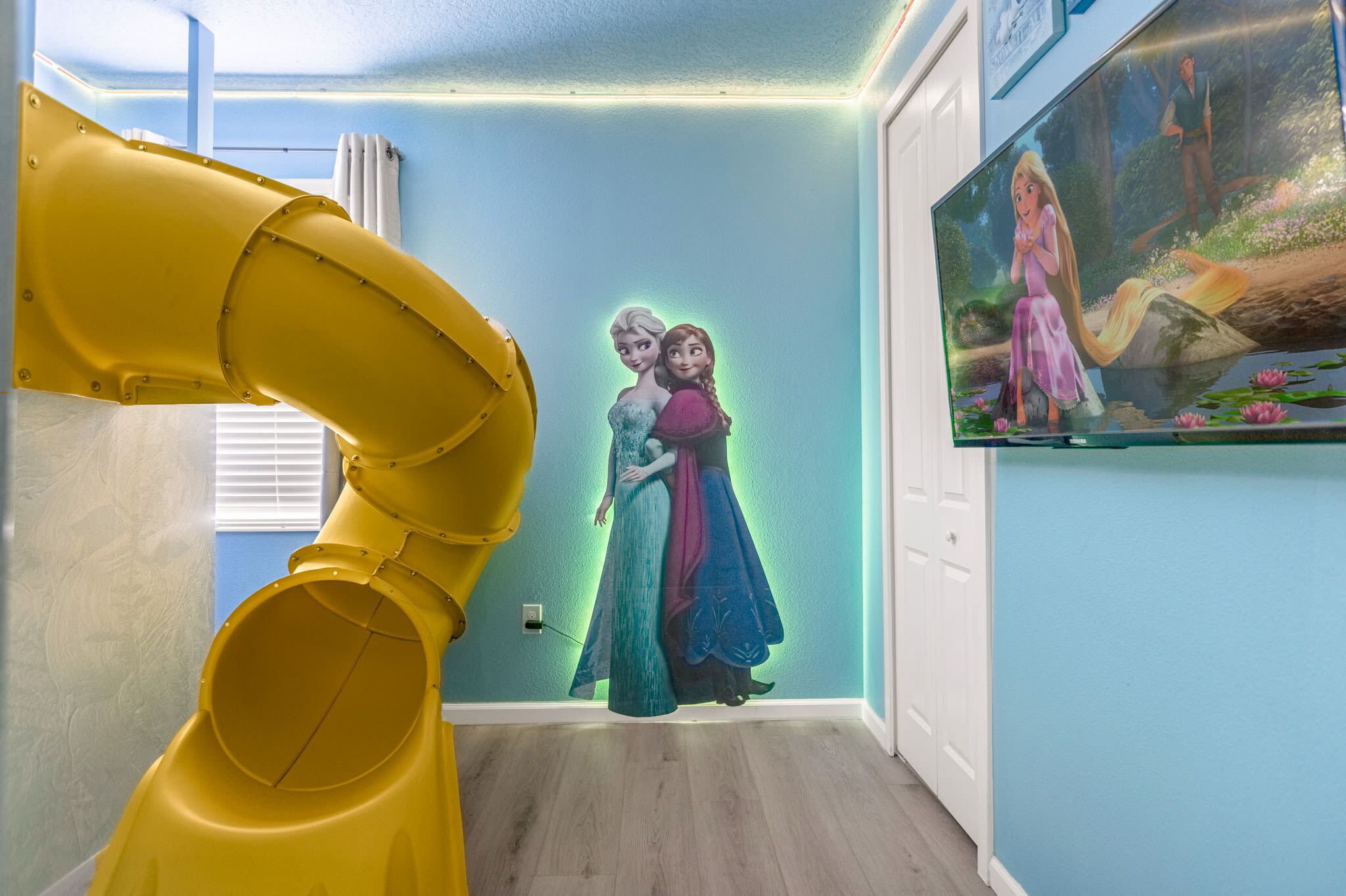 A room with a yellow play structure, a wall mural of animated characters, and a large poster of another animated character.