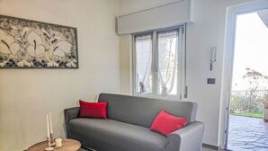 Harmaa sohva, jossa on punaiset koristetyynyt, pieni pyöreä pöytä, jonka päällä on kynttilöitä, ja seinällä oleva taulu.