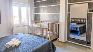 Huoneessa on vauvansänky, sänky, jossa on rullalle taiteltuja pyyhkeitä, ikkuna, jossa on verhot, ja vaatekaappi, jossa on peili.