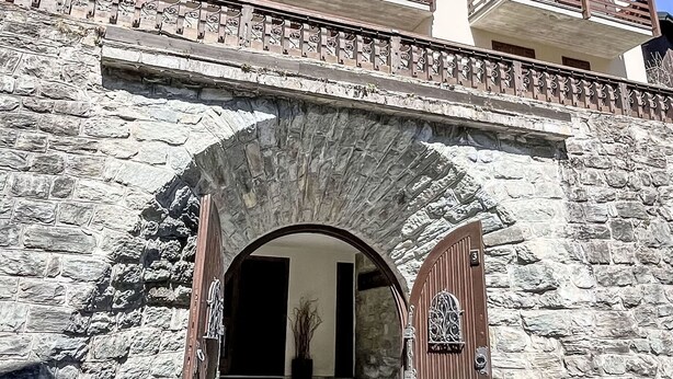 Um edifício de pedra com entrada arqueada, porta de madeira e varanda com grades.