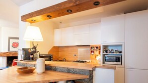 Cozinha moderna com armários brancos, bancada de madeira, micro-ondas embutido e uma parede decorativa em pedra.