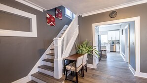 Un escalier avec des balustrades blanches, un coin repas avec une table et des chaises, et une cuisine en arrière-plan.