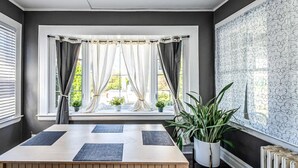 Une pièce avec une grande fenêtre, une table recouverte d’un tapis, des plantes en pot et un radiateur.
