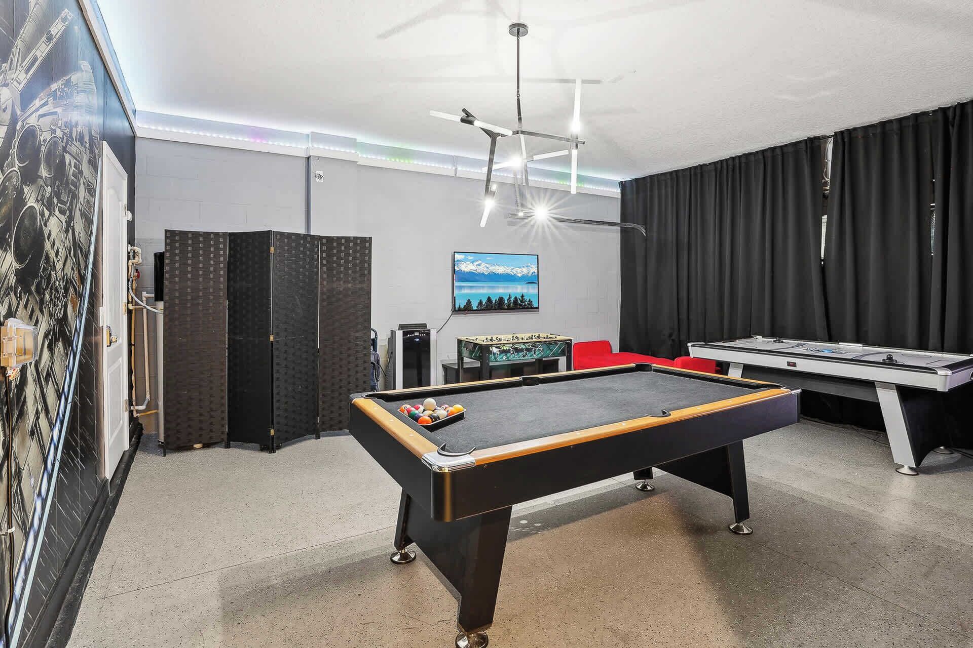 Ein Billardtisch mit Kugeln, ein Tischfu ßballspiel und ein Fernseher an der Wand.