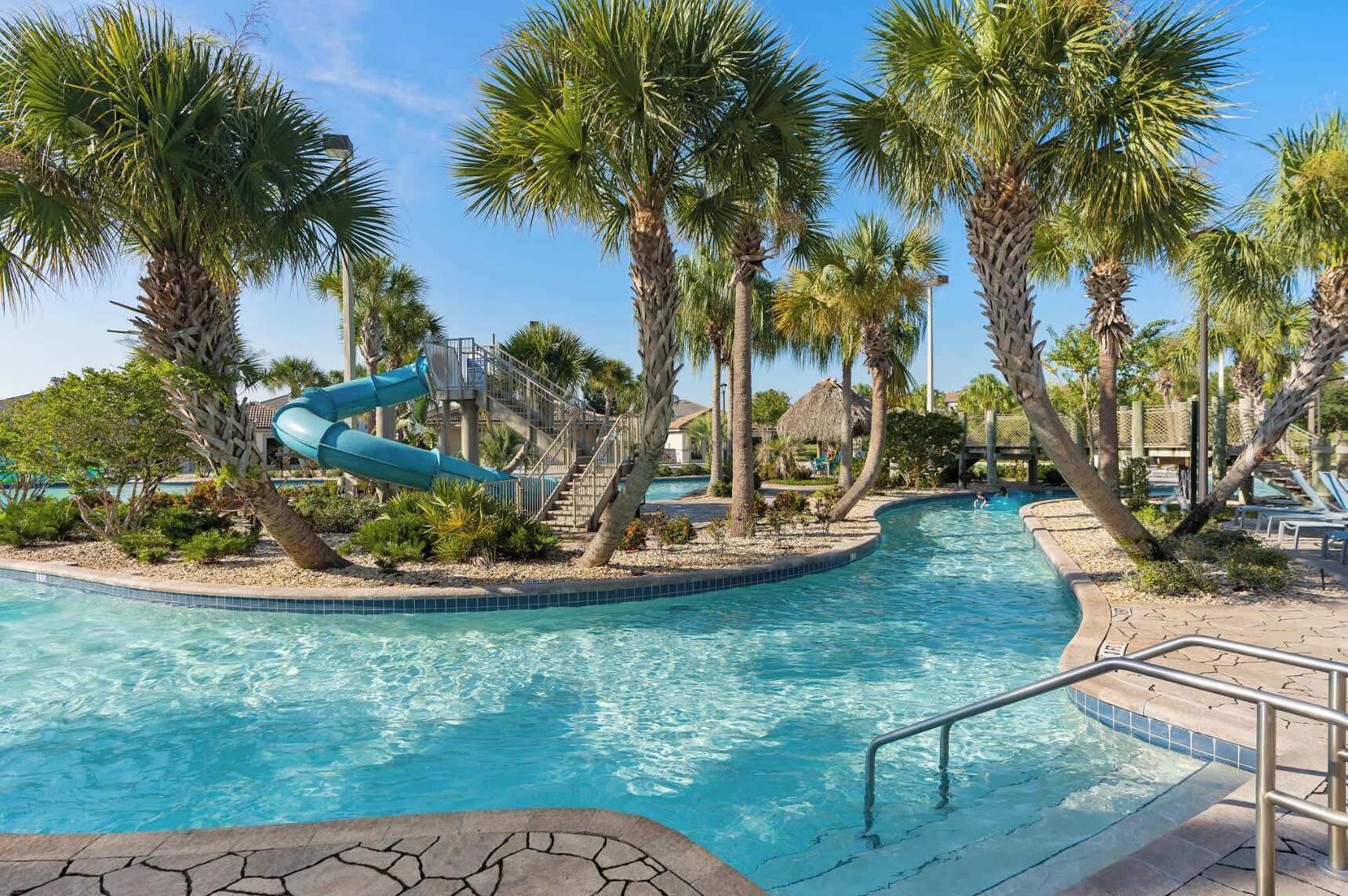A swimming pool with a water slide, surrounded by palm trees and lounge chairs.