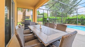 Een terras buiten met een eettafel en stoelen, een barbecue en een zwembad.