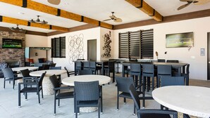 Een ruim buitenterras met meerdere tafels en stoelen, plafondventilatoren en een stenen openhaard.