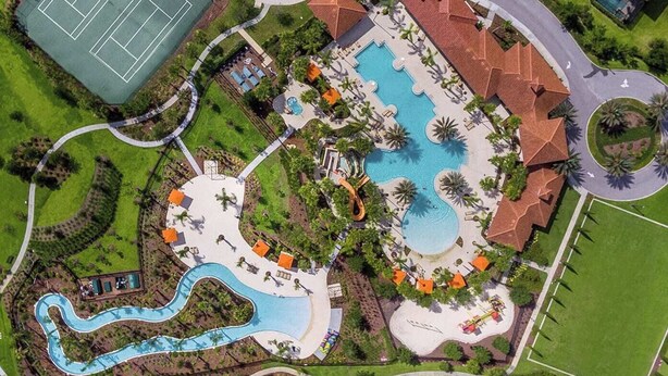 Luchtbeeld van een resort met een groot centraal zwembad, een apart tennisbaan en een kronkelende waterglijbaan.