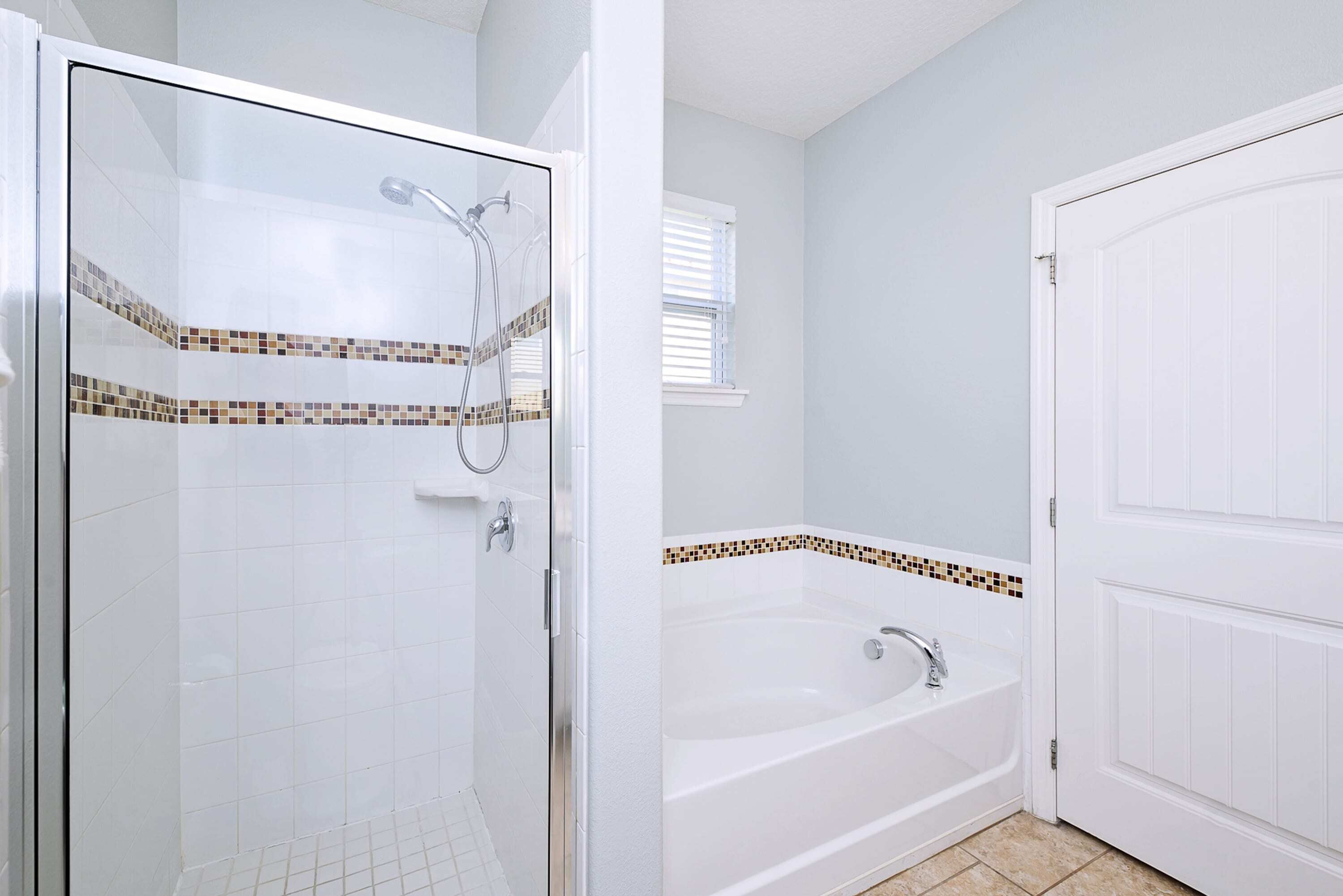 A bathroom with a glass-enclosed shower, a freestanding bathtub, and a white door.