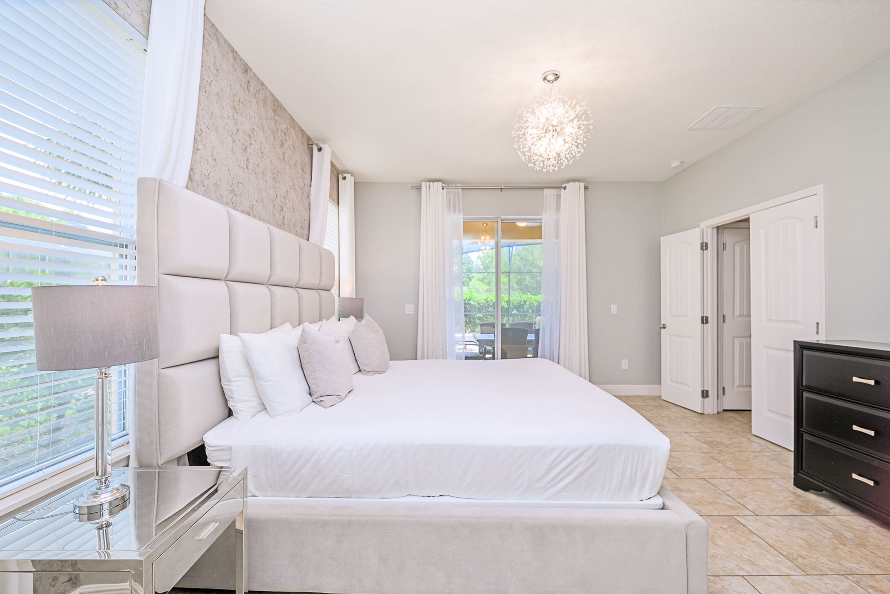 A modern bedroom with a large bed, a bedside table, a lamp, and a view of the outdoors through a window.