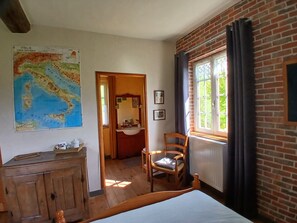 A room with a bed, wooden dresser, a map on the wall, a window with curtains, and a chair.
