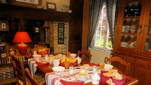 Comedor con una larga mesa dispuesta para una comida, sillas de madera, una lámpara roja y una pared de ladrillo adornada con cuadros.