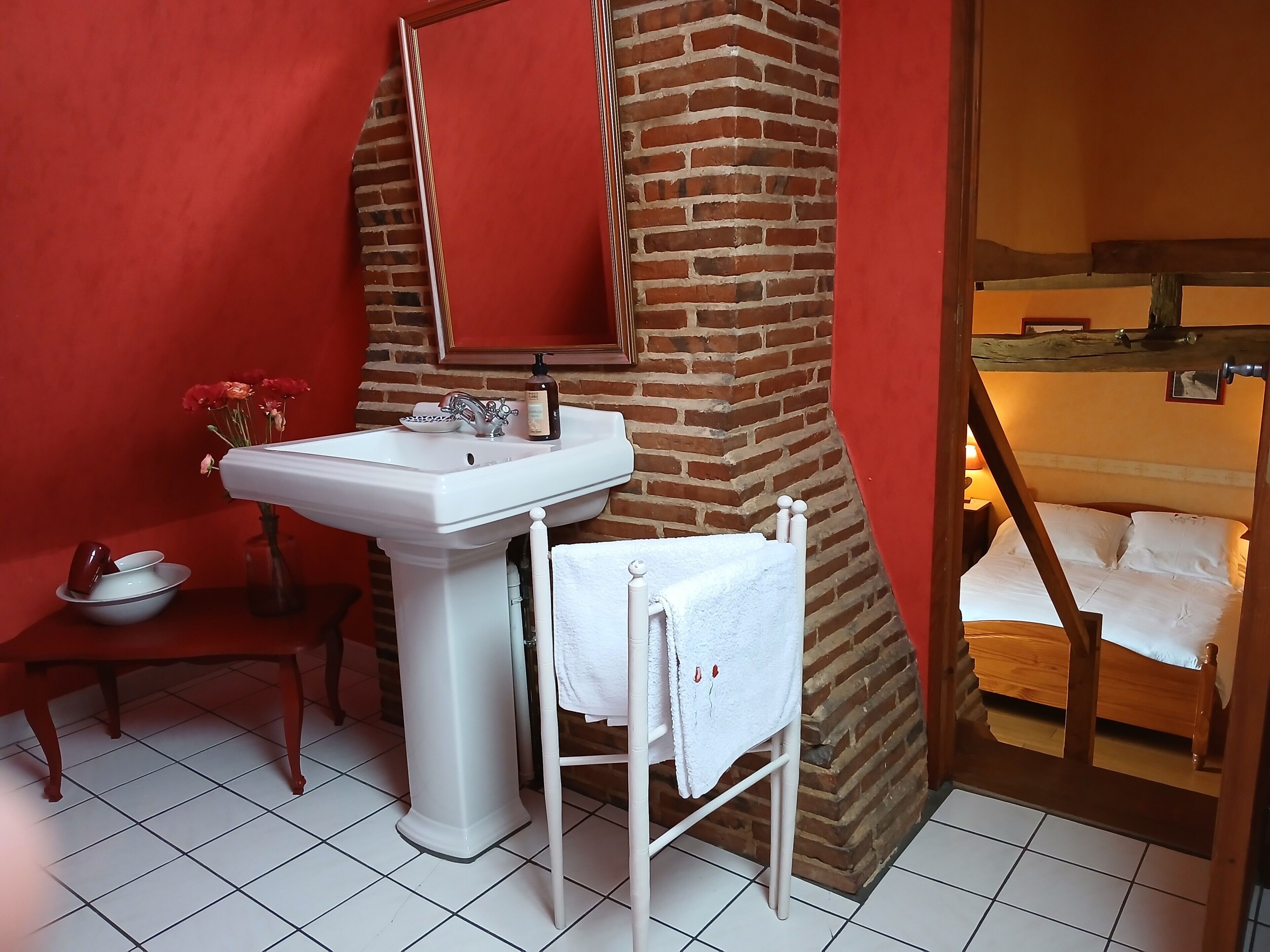 A bathroom with a white sink, a mirror, a towel rack, and a wooden bed.